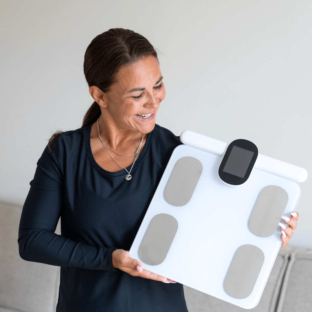 Sundhedsekspert smilende holder Kropsscanner Pro i hånden. Personlig sundhed og kropsanalyse derhjemme